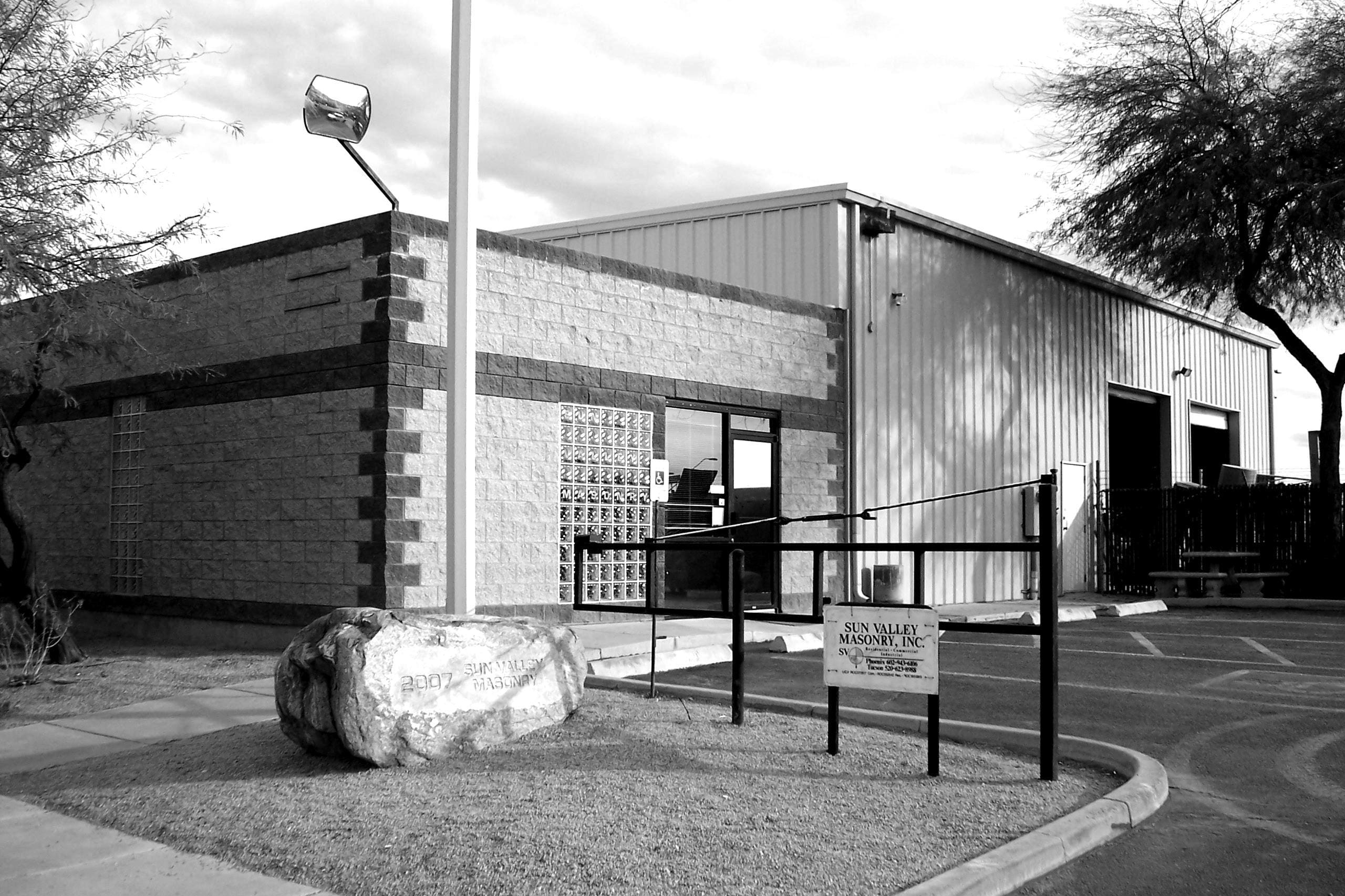 About Sun Valley Construction: A black and white photo of a single-story building with a glass brick window, metal sidings, and a handicap-accessible entrance, marked by railings and a sign that