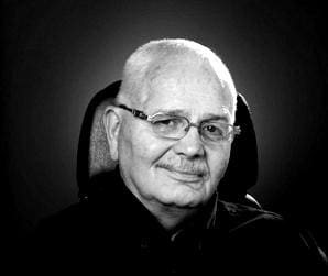 Black and white portrait of an elderly man with glasses, about Sun Valley Construction, smiling at the camera.