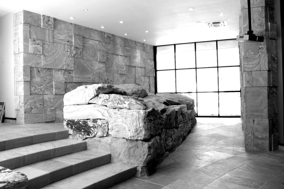 Modern interior by Sun Valley Construction featuring a natural rock formation integrated with architectural elements, with marble walls and floor-to-ceiling windows allowing natural light.