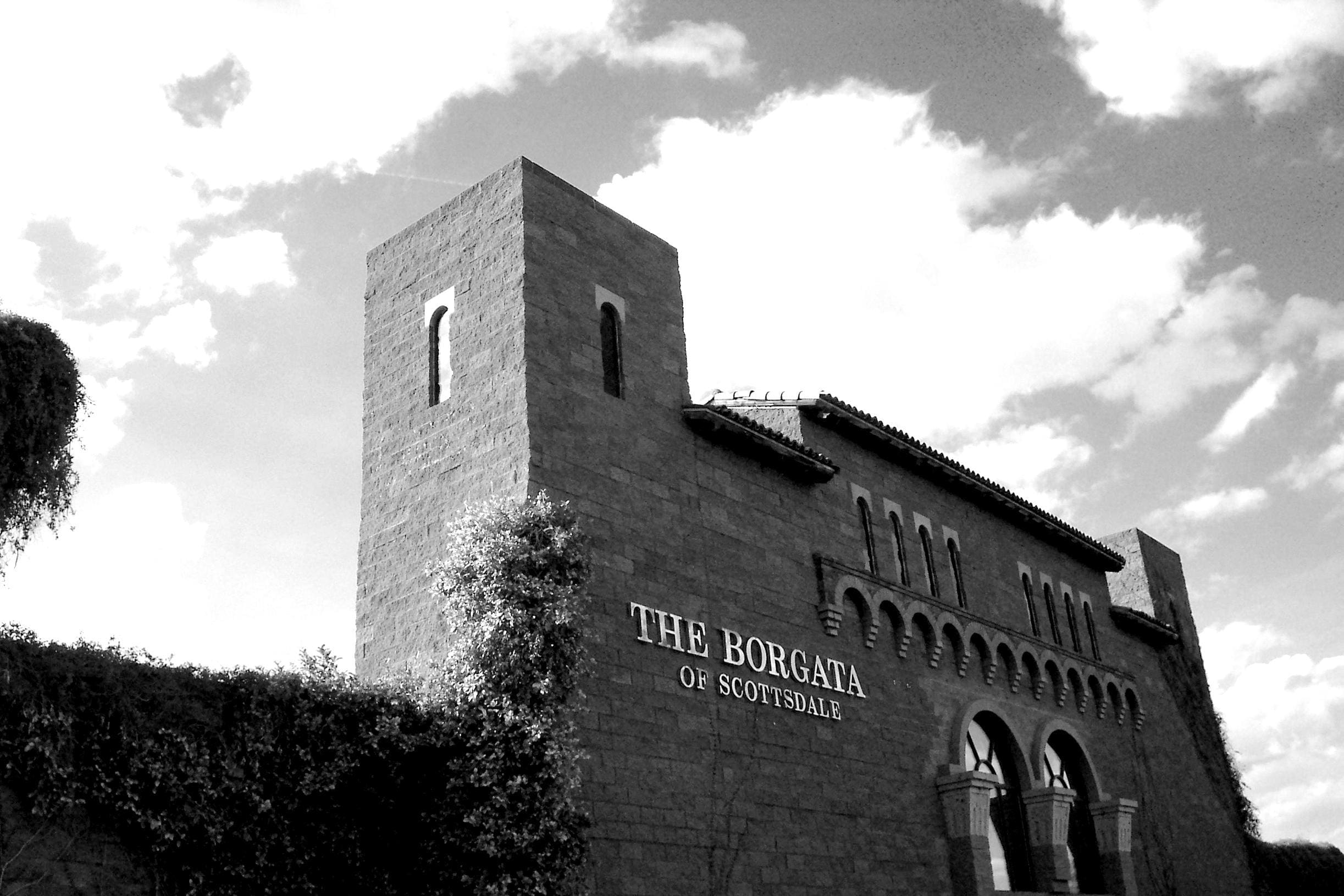 A black and white photograph of the Sun Valley Construction of Scottsdale building, adorned with a vine-covered wall, under a cloudy sky.