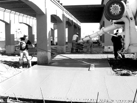 Construction workers from About Sun Valley Construction using a concrete pump to pour wet concrete at a construction site.