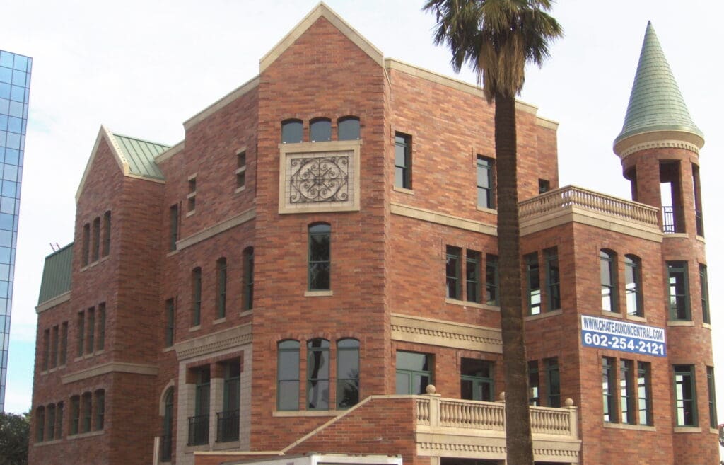 A red brick building with a conical tower, decorative stonework, and multiple arched windows, located under a partly cloudy sky.