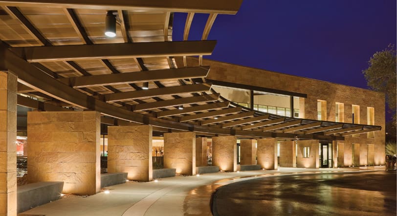 Modern building facade illuminated at night with an overhanging canopy and recessed lighting.