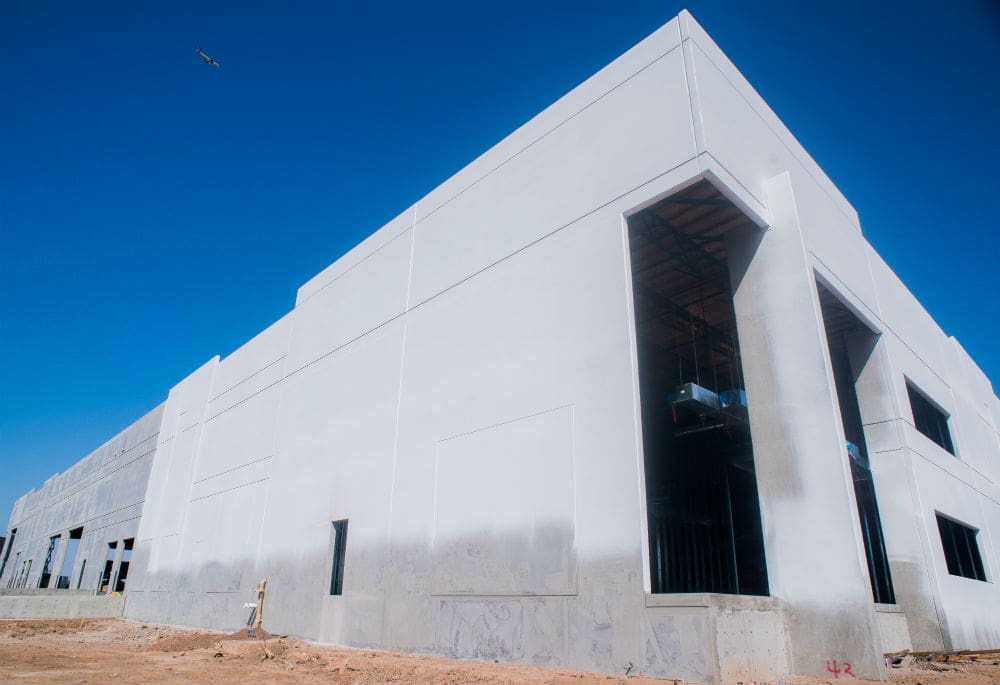 A partially constructed industrial building with large open doorways under a clear blue sky.