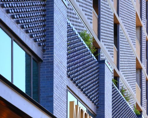 Close-up of the moontower building facade showing modern architectural design with a wooden overhang, large windows, and patterned metal balconies.