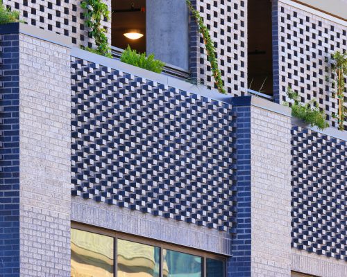 Close-up of a modern building facade with geometric brick design and balconies adorned with green plants.