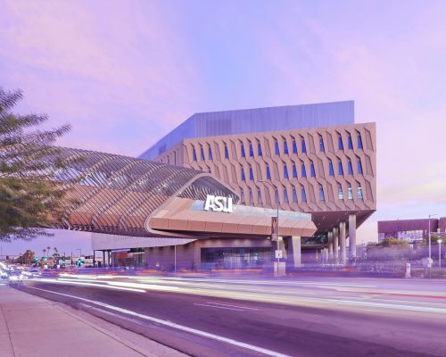 A modern asu building at twilight with a vibrant pink sky, lighting streaks from passing cars visible in front.