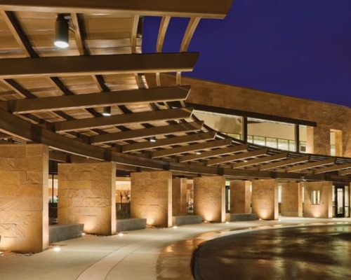 Modern building facade illuminated at night with an overhanging canopy and recessed lighting.