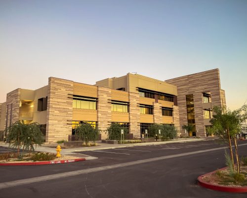 Modern multi-story office building at dusk with exterior lighting and a clear sky.