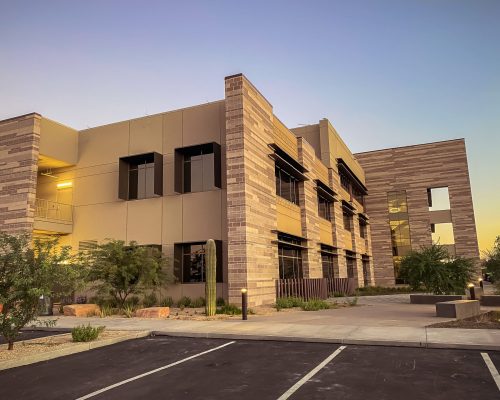 Modern office building exterior at dusk with illuminated windows and landscaped surroundings.