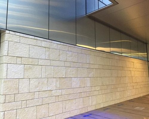 Exterior wall corner of a modern building with stone cladding and illuminated with strip lighting under an overhang, captured during dusk or dawn with a blue sky in the background.