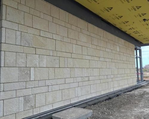 A section of a building under construction showing an insulated wall with stone veneer cladding and exposed structural elements on the right side.