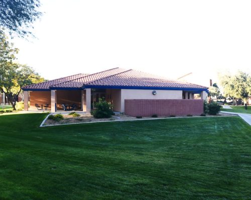 A single-story building with a brown tile roof and a wide lawn situated in a well-manicured park-like setting.