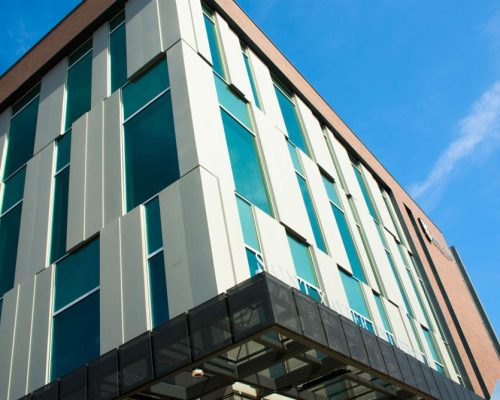 A modern building with a glass facade reflecting a clear blue sky.