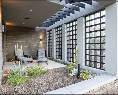 Residential home exterior featuring a covered patio with stylish seating and a decorative privacy screen.